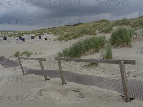 A wooden path through dunes leads to several beach chairs under a cloudy sky, juist, east frisia,