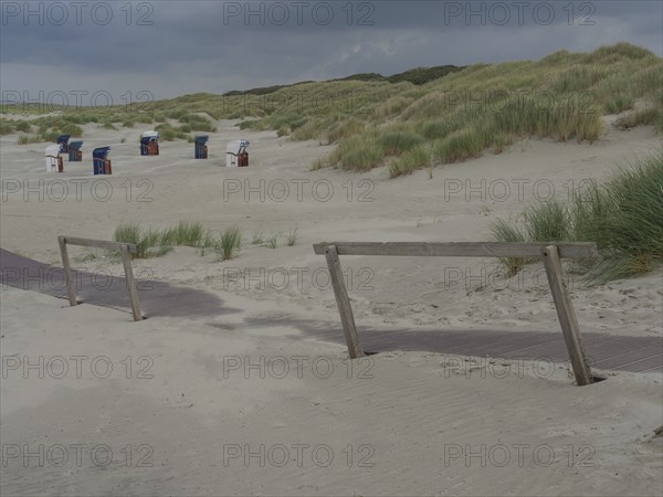 Deserted beach with a wooden path and scattered beach chairs under a cloudy sky, juist, east