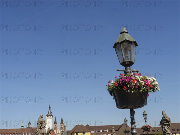 Flower hanging basket on a lantern in front of a historic backdrop and blue sky, Würzburg, Bavaria,