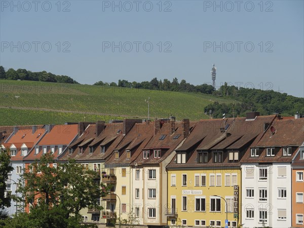 Row of colourful houses in front of green vineyards and a television tower on the horizon,