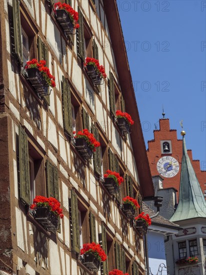 Half-timbered house with flower boxes full of red flowers and shutters, in the background a church