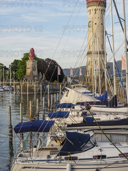 Boats in the harbour with lighthouse and lion sculpture in the background on a sunny day,