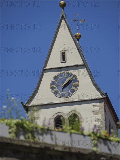 Close-up of a church tower with clockwork and spire against a clear blue sky in the sunshine,