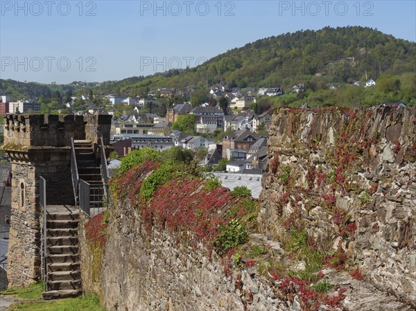 Historic tower and castle wall overlooking a green, hilly urban landscape on a sunny day, Saarburg,