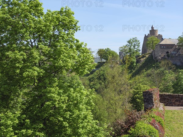 A castle and ruins hidden between green trees, embedded in nature under a clear sky, Saarburg,