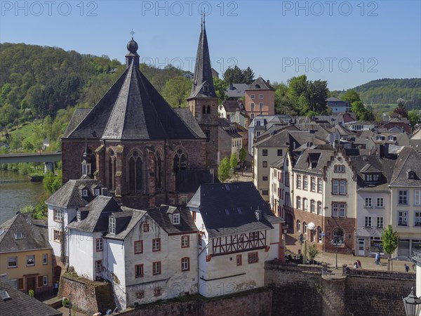 View of a historic town with churches and half-timbered houses next to a river in sunny weather,