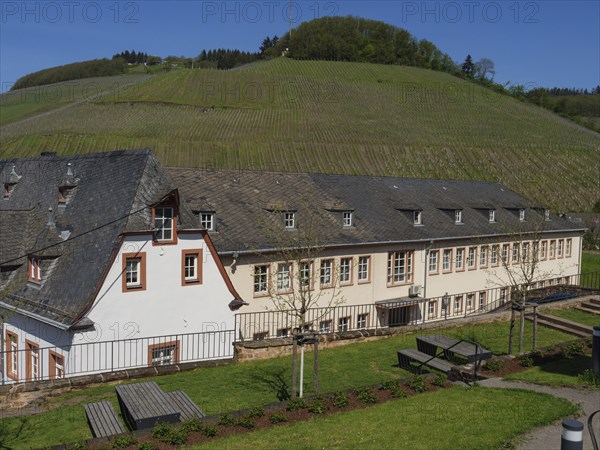 Large building in the middle of a rural, hilly landscape with meadows and trees in sunny weather,