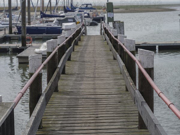 A wooden footbridge with railings leads down to a quiet harbour, Spiekeroog, East Frisia, GERMANY
