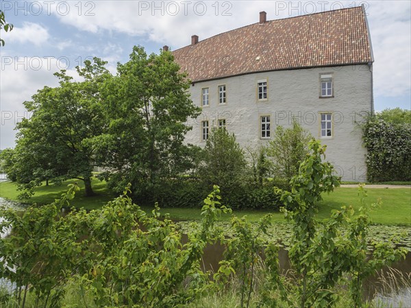Historic castle building with red tiled roof, surrounded by green trees and a pond, Steinfurt,