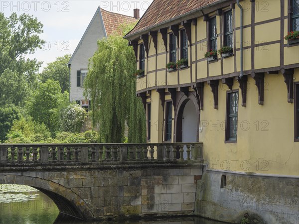 Historic building on the waterfront with a bridge, willow and flowering windowsills, Steinfurt,
