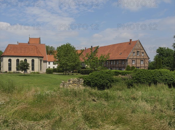 View of an estate with a church, tiled roofs, surrounded by lawns and trees under a blue sky,