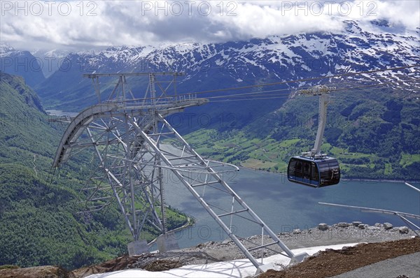 Modern cable car crossing a fjord and green valleys with snow-capped mountains in the background,