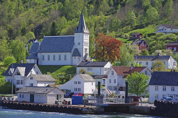 Village with church on a green hill, surrounded by wooden houses and a ferry pier, Utne, Hardanger,