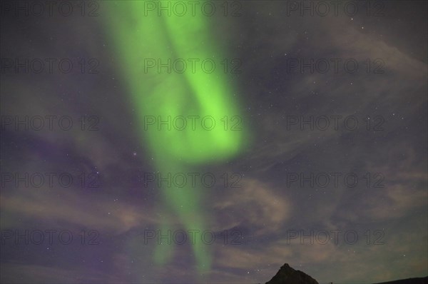 Green Northern Lights stretching across a mountain landscape against a starry night sky, Nyksund,
