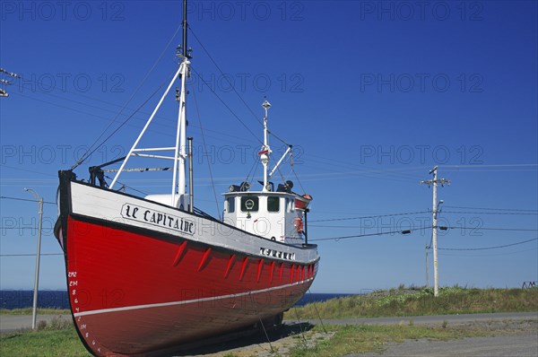 Red boat on land next to a coastal road under a clear blue sky, Gaspesie, St. Lawrence River,