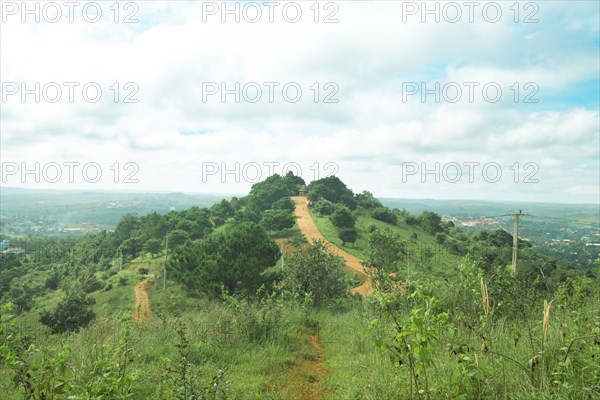 A serene hill with a winding path surrounded by lush greenery under a partly cloudy sky in the
