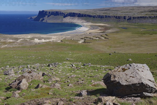 A vast coastal panorama with green hills and rugged cliffs, bordering a deep blue sea, Latrabjarg,