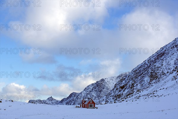 A lonely red house in the middle of a snowy winter landscape in front of majestic mountains,