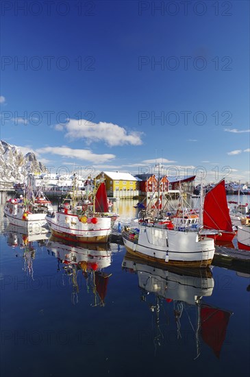 Fishing boats with red sails lying calmly on the quay, reflected in the water, surrounded by