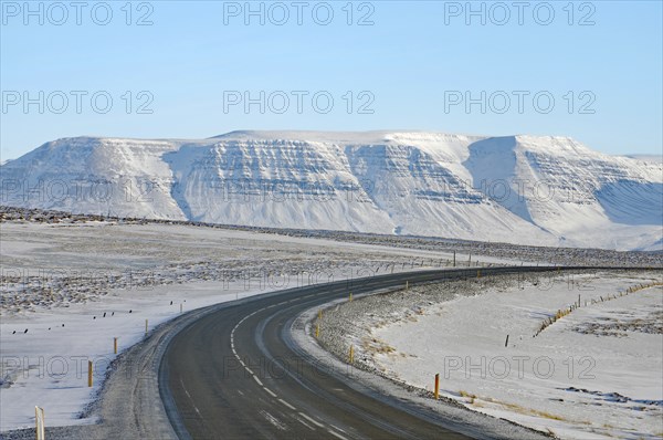 Snowy road leads to a snow-covered mountain range under a clear blue sky, Ring Road, North Iceland,