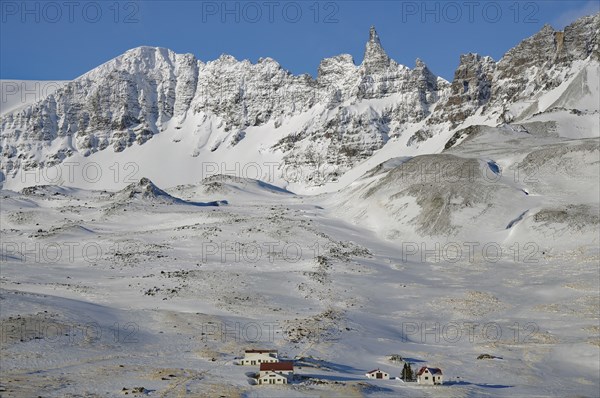 Snow-covered mountains with small houses in the foreground under a clear blue sky, winter,