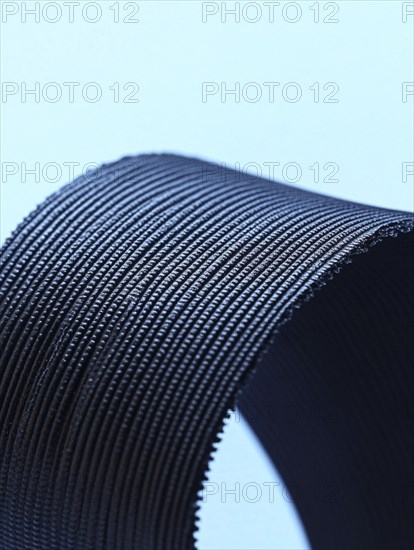 Close-up abstract shot of a textured black ribbon against a blue background, AI generated