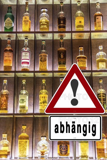 Shelf full of alcohol bottles with a warning sign about alcohol addiction, illuminated in a bar
