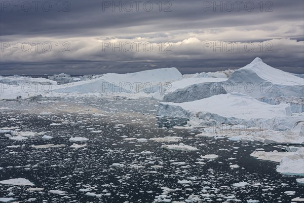 Icebergs in a fjord against a cloudy sky, summer, Ilulissat Icefjord, Disko Bay, West Greenland,