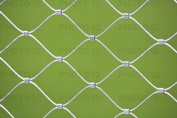 Mesh screen made of interwoven metal cables. The background is a uniform green colour. This image