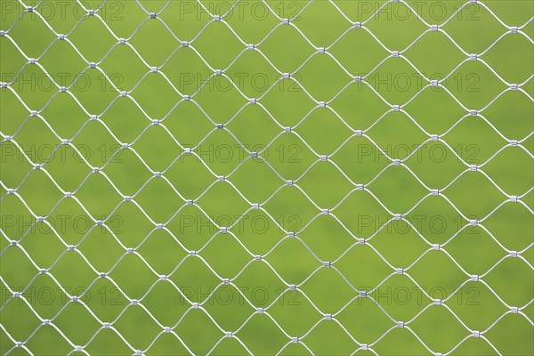 Mesh screen made of interwoven metal cables. The background is a uniform green colour. This image