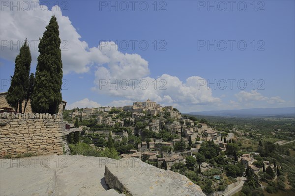 View of townscape with cypresses and rocks, mountain village, Gordes, Luberon, Vaucluse, Provence,