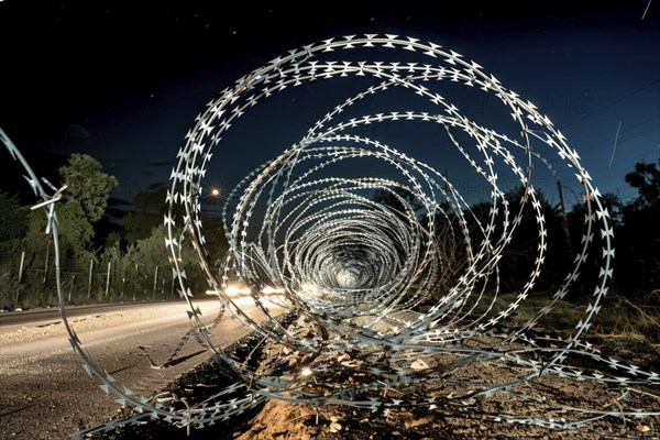 Spiral barbed wire installation alongside a road at night, creating a dramatic, secure environment,