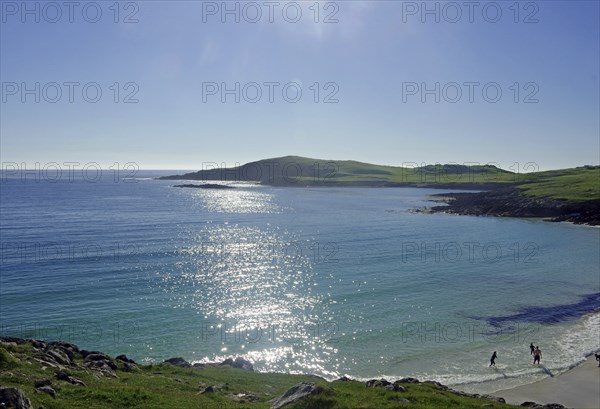 Sparkling sea with a rocky coastline, tranquil atmosphere and people on the beach, Scalloway,