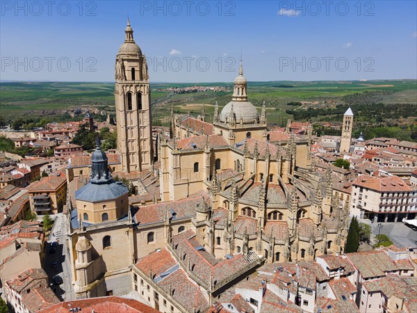 Aerial view of a historic city with a large church and red roofs under a clear blue sky, surrounded