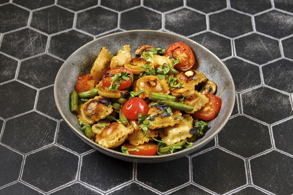 Fried ravioli with green beans, tomato and champignon mushrooms in a plate
