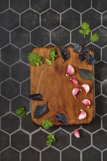 Overhead composition with place for text with wooden chopping board with basil, garlic and cilantro