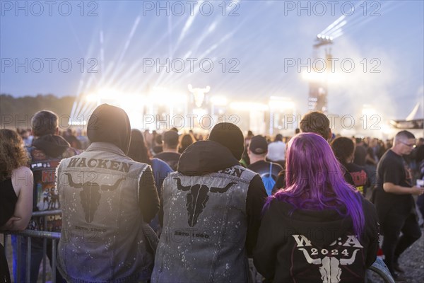 Festival visitors with Wacken jackets look at the two main stages Faster and Harder at dusk at the