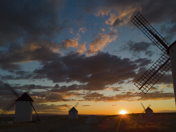 Several windmills in front of a dramatic sunset with colourful sky and clouds, creating a calm and