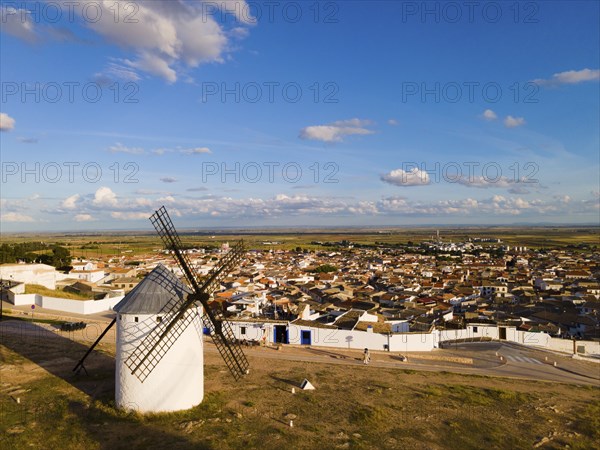 Windmill overlooking a Spanish town, nestled in a vast landscape under a clear blue sky with a few