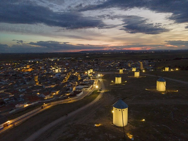 Illuminated windmills and a village in the light of dusk. The sky shows bright colours of the