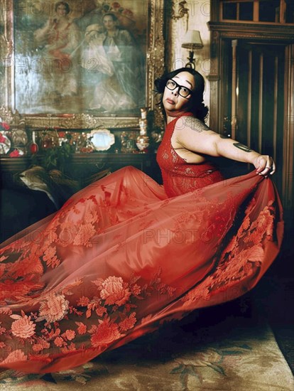 Woman in a flowing red dress with floral patterns, in an ornate and luxurious room featuring a