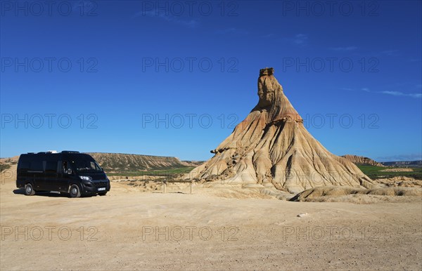 Motorhome in a barren desert landscape with striking rock formations and a clear blue sky,