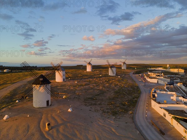 Landscape at sunset with windmills and a road leading to an illuminated village, aerial view,