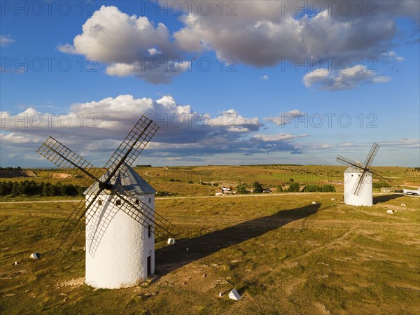 Two windmills stand in a wide landscape under a partly cloudy blue sky, aerial view, windmills,