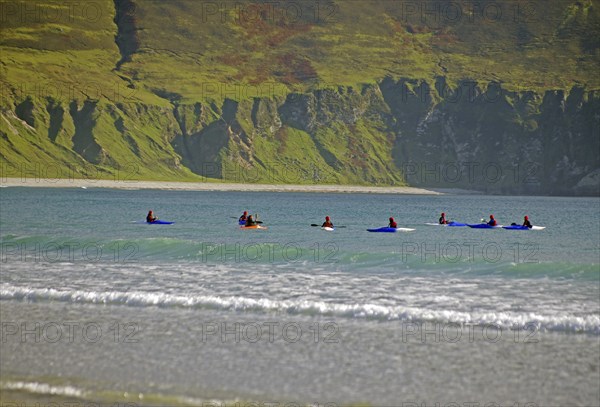 Group of surfers on their boards on the sea near rocky shore, Achill Island, County Mayo, Ireland,