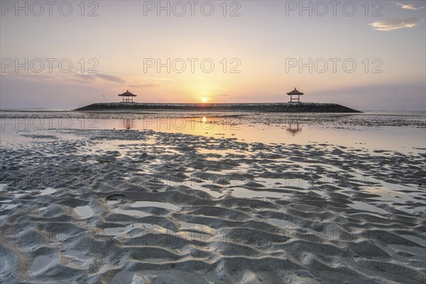 Fantastic sunrise on the beach with small temples. View of the sea as far as the horizon. Sanur,