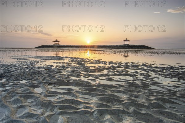 Fantastic sunrise on the beach with small temples. View of the sea as far as the horizon. Sanur,