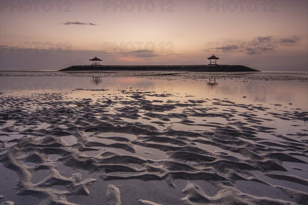 Fantastic sunrise on the beach with small temples. View of the sea as far as the horizon. Sanur,