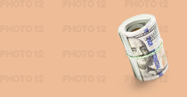 Roll of one hundred dollar bills secured with a rubber band on a peach fuzz background
