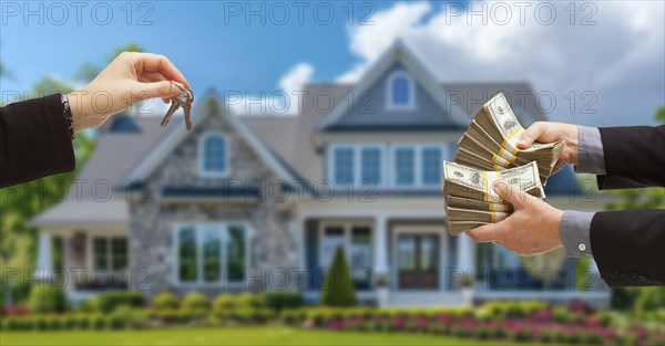Real estate agent handing over house keys for stacks of money in front of new house